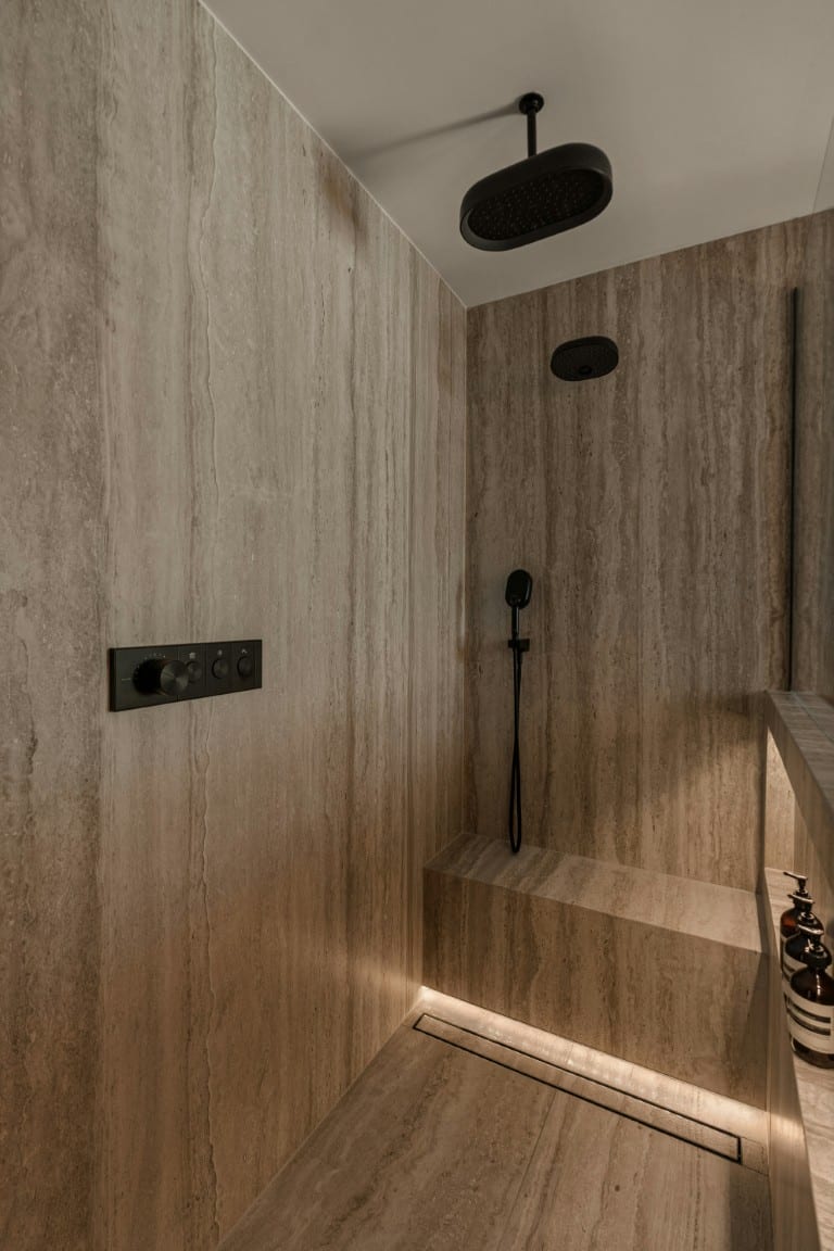 Travertine shower with black rainfall showerhead and integrated bench